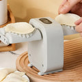 The dumpling maker machine with a dumpling dough on one mould and someone placing another on the second mould.