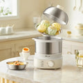 The egg boiler machine on a bench top in a kitchen next to a bowl of shrimp soup and a cooked egg. The lid of the machine is removed to reveal dumplings and pastries that are cooking.