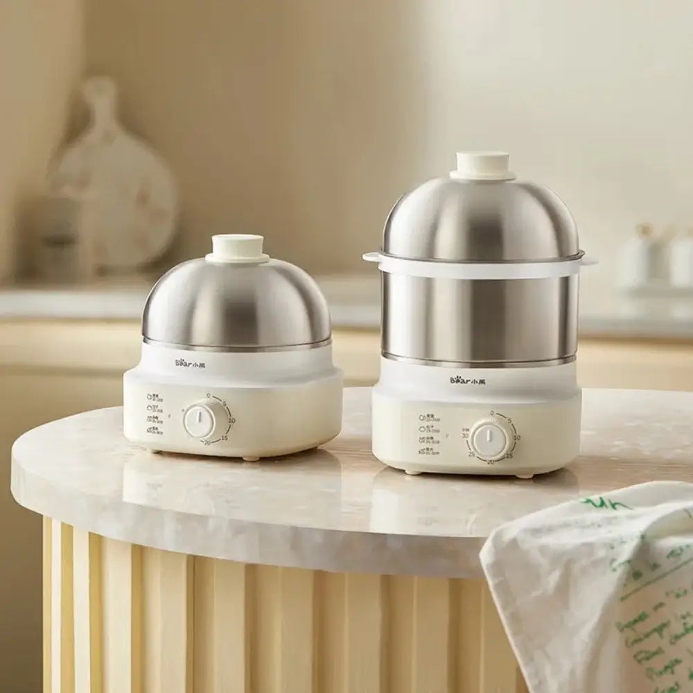 The electric egg cookers both different sizes, sitting on a kitchen bench.