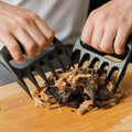 Both meat shredding claws being used by a man to pull pork.